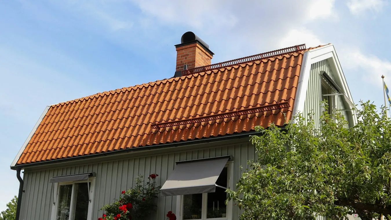 Nylagt tak med röda tegelpannor, snörasskydd och murad skorsten på en grön villa